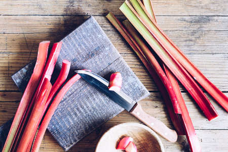 Bundle of fresh picked stalks of organic rhubarb on cutting board with knife on a wooden background....