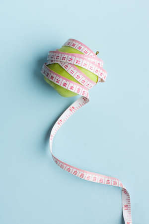 Apple with measuring tape on blue background. Weight loss, counting calories and healthy eating concept - calculate daily nutrition intake. Top view. Copy space.の写真素材