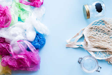 Many disposable plastic bags vs reusable cotton bag and glass jars on a blue background. Zero waste shopping. Sustainable living, plasticfree concept. Eco friendly plastic free items. Top view.の写真素材