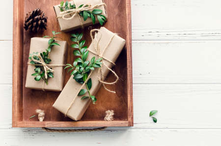 Modern Christmas wrapped presents with natural decor on white wooden background. Gifts boxes in craft paper with twine and green branches. Seasonal greetings card. Top view. Flat lay. Copy space.の写真素材