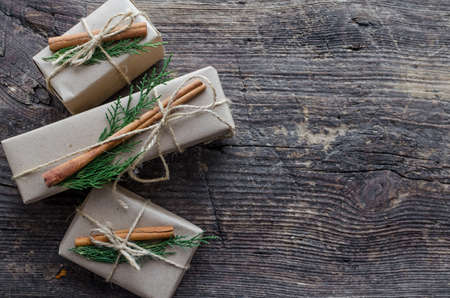 Modern Christmas wrapped presents with natural decor on wooden background. Gifts boxes in craft...