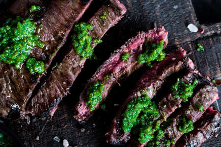 Juicy steak medium rare beef with spices and pesto sauce on wooden board on black background. Top view.の写真素材