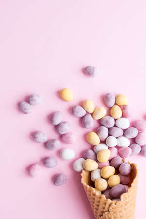 Flat-lay of waffle sweet ice cream cone with Easter mini chocolate eggs over pastel light pink...