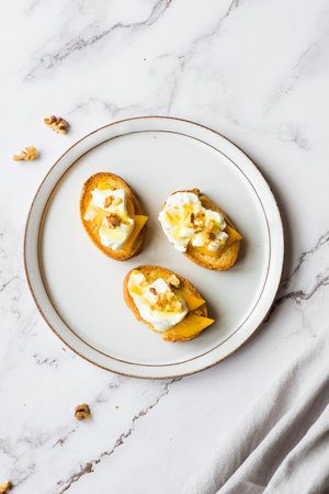 Baguette slices with cream cheese, persimmon, honey, and nuts on marble background. Bruschetta antipasti. Sweet savory taste, gourmet appetizer recipe idea. High quality photo.の写真素材