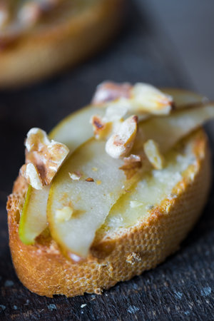Appetizer bruschetta with pear, honey, walnut and blue cheese on black background. Sweet toast with pear, cheese and honey. Healthy snack or breakfast. High quality photo.の写真素材