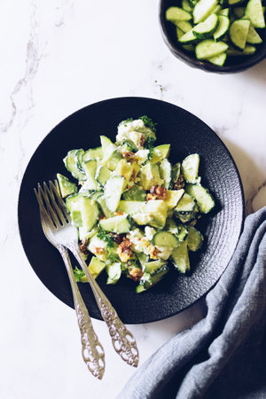 Healthy salad with fresh vegetables - cucumber, avocado, walnuts, feta cheese and coriander on a...