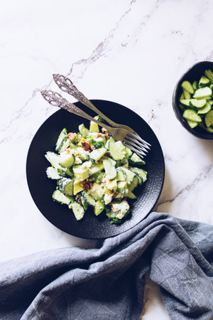 Healthy salad with fresh vegetables - cucumber, avocado, walnuts, feta cheese and coriander on a bowl.の写真素材
