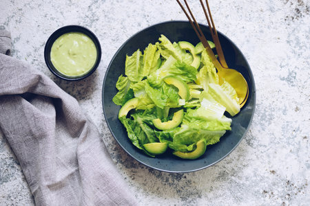 Healthy green salad with fresh vegetables - avocado and lettuce salad leaves on a black plate.の写真素材