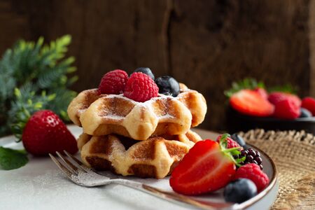 Belgian waffles with strawberries, summer berries on plate with canvas on dark old wooden dramatic...