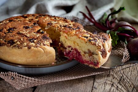 Homemade delicious beetroot pastry tart on kitchen grill with slice of cake and fresh beetroots on rustic wooden bakground. Menu, board, banner. Vintage traditional rustic kitchen. British mealの写真素材