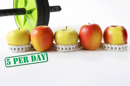 Healthy life concept. Multicolored apples with measure tap and ab wheel on white background