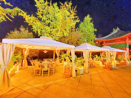 Outdoor restaurant in the garden with tables and chairs on the terrace at sunset,  decorated with light bulbsの写真素材