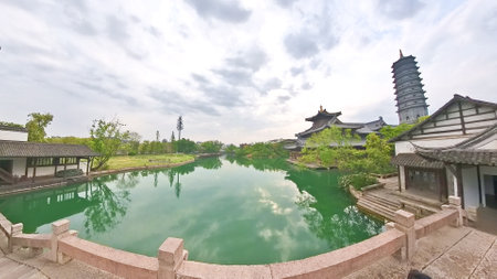 A tall, ornate pagoda rises above traditional rooftops and lush greenery under a bright sky, symbolizing serenity and historical beauty.の写真素材