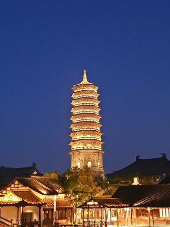 A beautifully illuminated pagoda and traditional Chinese buildings reflect on calm waters under a deep blue night skyの写真素材