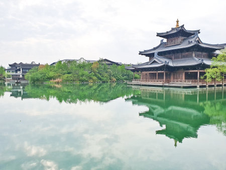 Traditional Chinese riverside houses reflect on calm green water, with a pagoda tower and lush trees completing the serene sceneの写真素材
