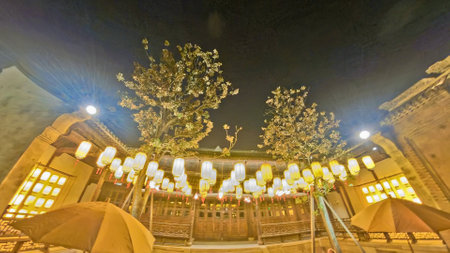 Traditional Chinese wooden building with intricate carvings, illuminated by glowing lanterns hanging above, creating a warm, festive nighttime ambianceの写真素材