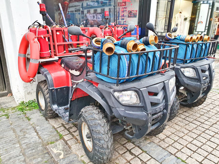 Two red quad bikes equipped with fire extinguishers, hoses, and rescue gear, parked on a cobbled...