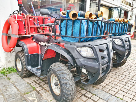 Two red quad bikes equipped with fire extinguishers, hoses, and rescue gear, parked on a cobbled...