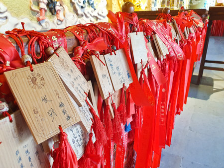 Wooden wishing plaques and red prayer ribbons with handwritten messages are tied together in a temple, symbolizing blessings and hopesの写真素材