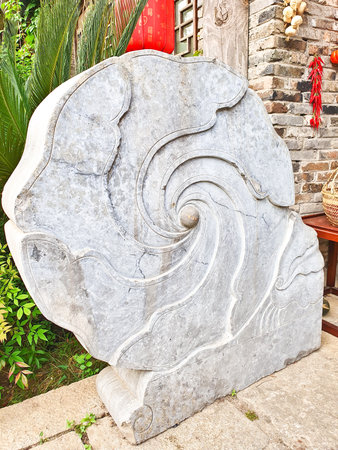 A beautifully carved stone sculpture featuring a swirling spiral design, set against a traditional brick wall with vibrant decorationsの写真素材