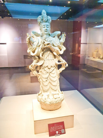 A detailed white statue of a multi-faced deity with many arms, standing gracefully on a lotus pedestal in a museum.の写真素材