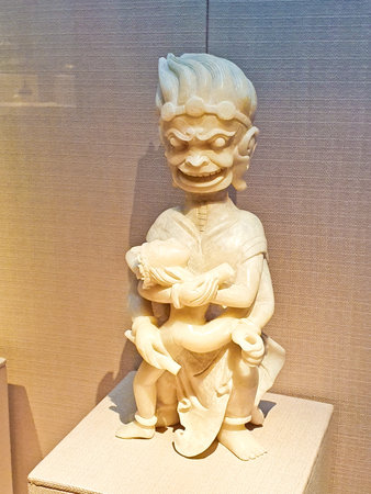 A fierce statue with exaggerated features holds a smaller figure, showcasing intense emotion and energy in an indoor museum setting.の写真素材