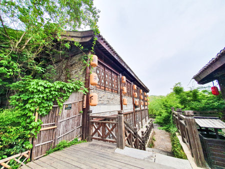 Traditional Chinese tea house with wooden architecture, hanging lanterns, outdoor seating, and cobbled stone path surrounded by lush greeneryの写真素材