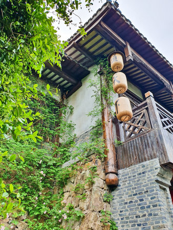 Traditional Chinese tea house with wooden architecture, hanging lanterns, outdoor seating, and cobbled stone path surrounded by lush greeneryの写真素材