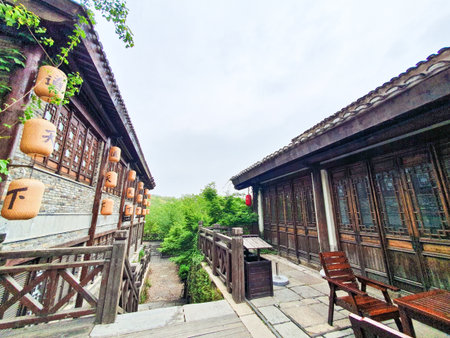 Traditional Chinese tea house with wooden architecture, hanging lanterns, outdoor seating, and cobbled stone path surrounded by lush greeneryの写真素材