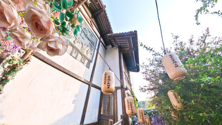 Traditional Chinese tea house with wooden architecture, hanging lanterns, outdoor seating, and cobbled stone path surrounded by lush greeneryの写真素材