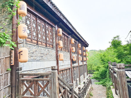 Traditional Chinese tea house with wooden architecture, hanging lanterns, outdoor seating, and cobbled stone path surrounded by lush greeneryの写真素材