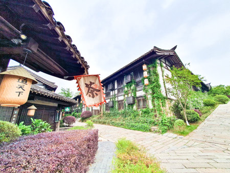 Traditional Chinese tea house with wooden architecture, hanging lanterns, outdoor seating, and cobbled stone path surrounded by lush greeneryの写真素材