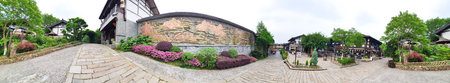 A peaceful stone path runs beside a decorative wall with mountain carvings, bordered by lush greenery and traditional architectureの写真素材