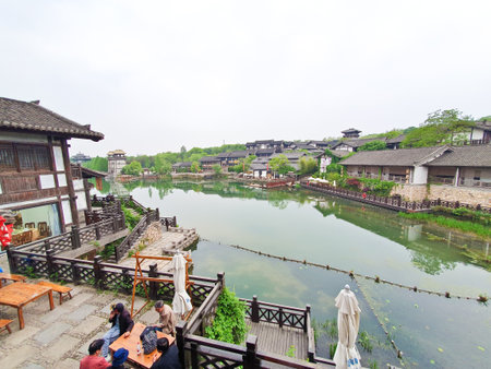 A tranquil canal scene at dusk with traditional Chinese buildings, soft lights reflecting in water, surrounded by nature and architectureの写真素材