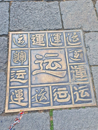 A decorative bronze plaque with various Chinese characters is embedded in a stone pavement, showcasing calligraphy styles and symbols for "luck".の写真素材