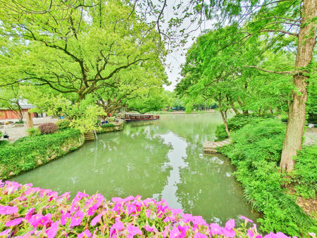 A scenic view of a tranquil pond surrounded by lush greenery, vibrant flowers, and a traditional...
