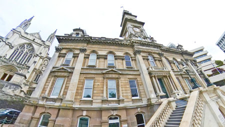 A grand brick and stucco building with columns and a teal door stands proudly under a cloudy sky