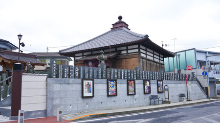 A traditional Japanese shrine with stairs and lanterns sits on a street corner, with modern buildings and a van in the background.の写真素材