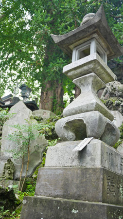 A grand, weathered bronze lantern stands in the center, flanked by smaller, ornate stone lanterns, with lush green trees in the backgroundの写真素材