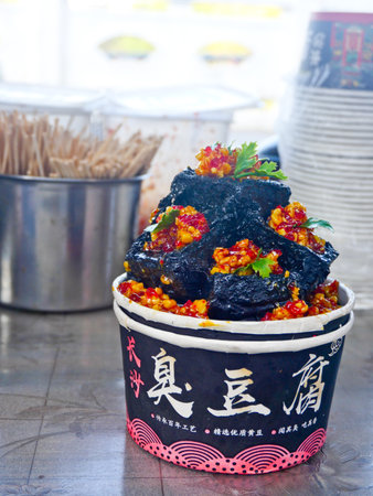 a pile of deep-fried black Stinky tofu pieces, stacked high in a disposable paper cupの写真素材
