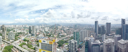 A wide daytime cityscape showing dense urban buildings, tall modern towers, distant mountains, and...