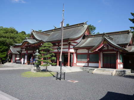 The main shrine hall, featuring a gray tiled roof and red trim with visitors on a sunny dayの写真素材