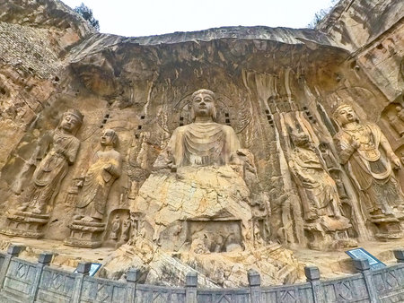 Longmen cliff carvings featuring central Buddha with bodhisattvas, intricate halos, and weathered...