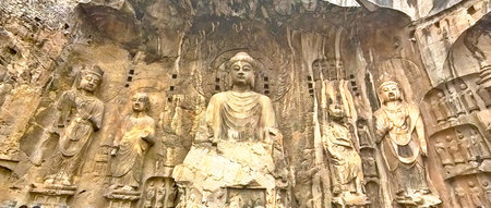 Longmen cliff carvings featuring central Buddha with bodhisattvas, intricate halos, and weathered...
