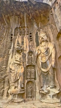 Longmen cliff carvings featuring central Buddha with bodhisattvas, intricate halos, and weathered...