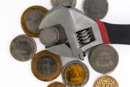 Pile of Colombian money coins and an adjustable wrench on a white background.の写真素材