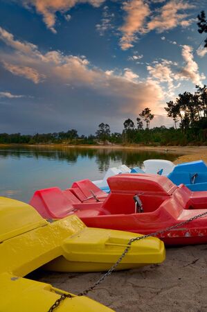 Pedal boats of various colours lined up at lake bankの写真素材