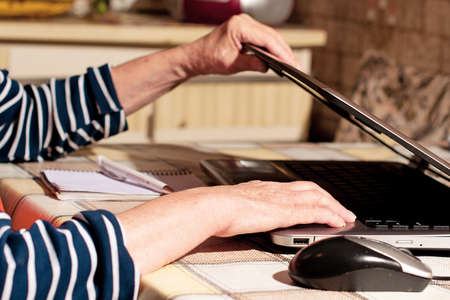 Hands of an elderly woman opened laptop