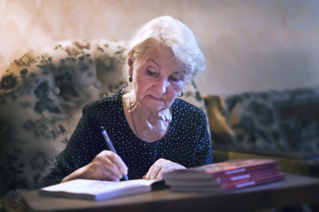 elderly woman writing at a table in his apartmentの写真素材