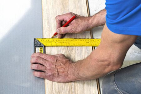 hands of a carpenter measuring wood laminate flooring